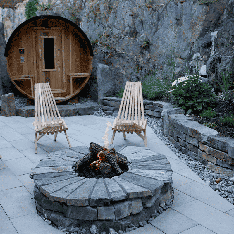 Wood chairs and a fire pit with a barrel sauna in the background
